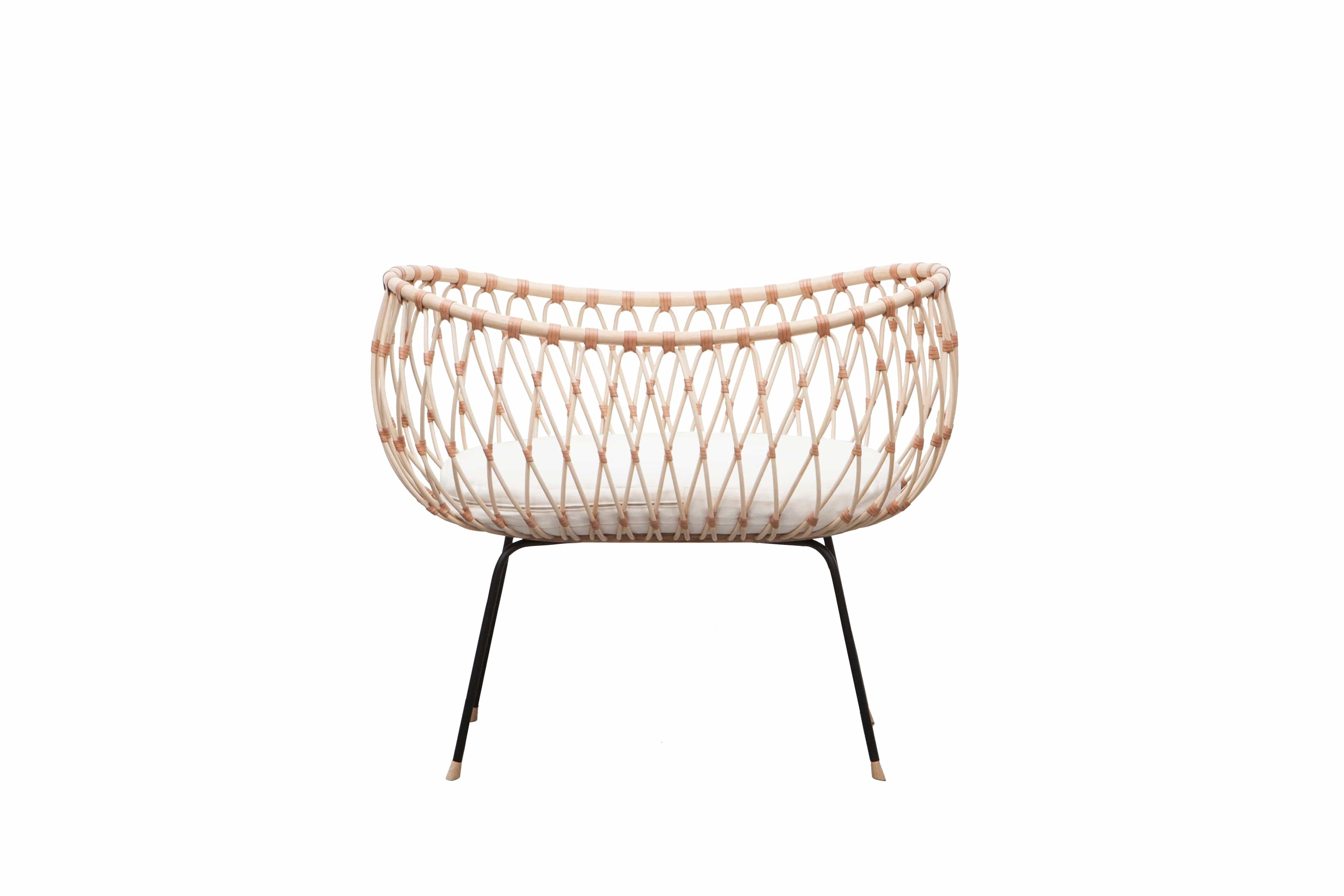 Round crib with outwards curved basket. Made of woven, light beige rattan beams, connected with light brown leather straps and standing on slim black metal legs.