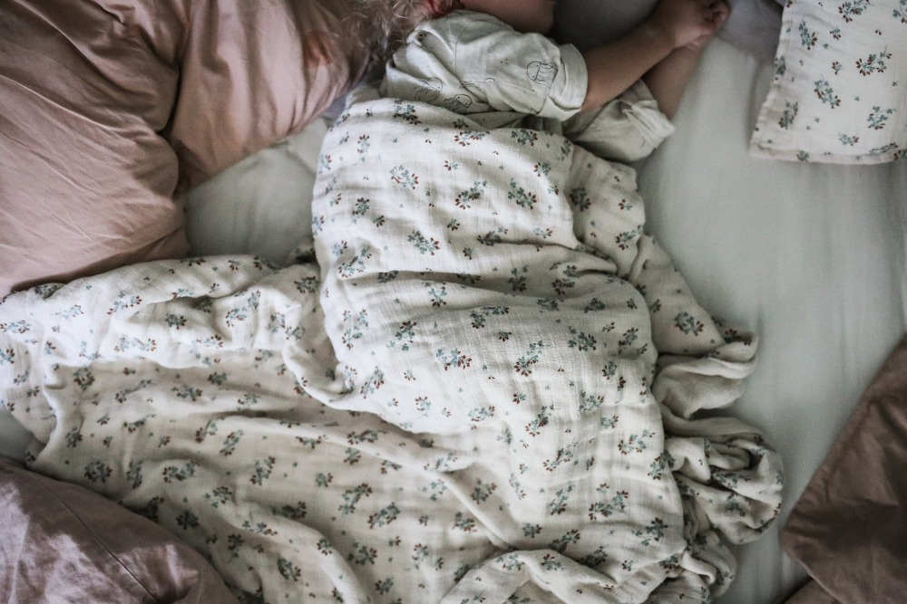 Baby lying in bed covered with cotton bedding with clover pattern