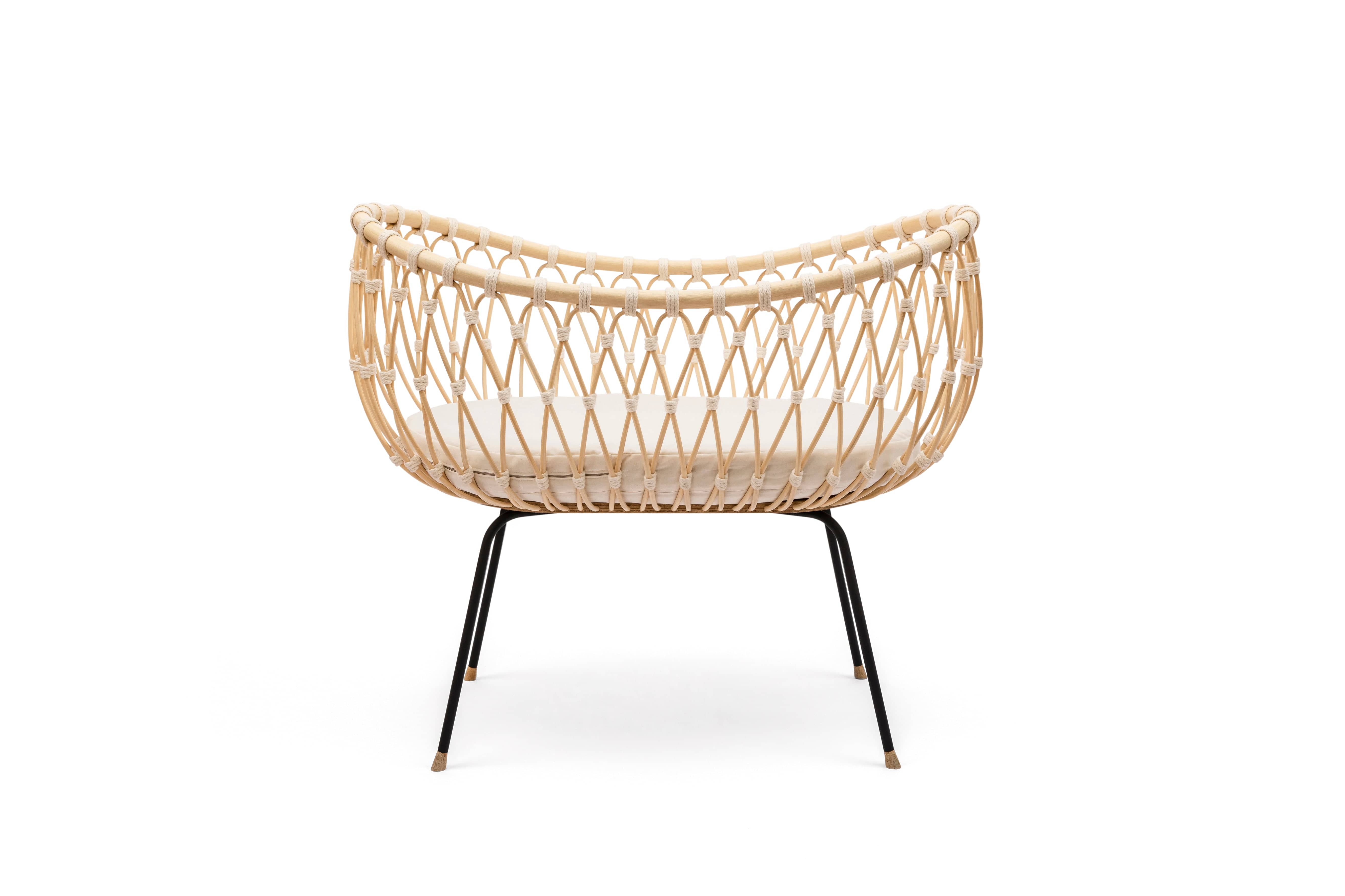 Round crib with outwards curved basket. Made of woven, light beige rattan beams, connected with off-white cotton strings and standing on slim black metal legs.