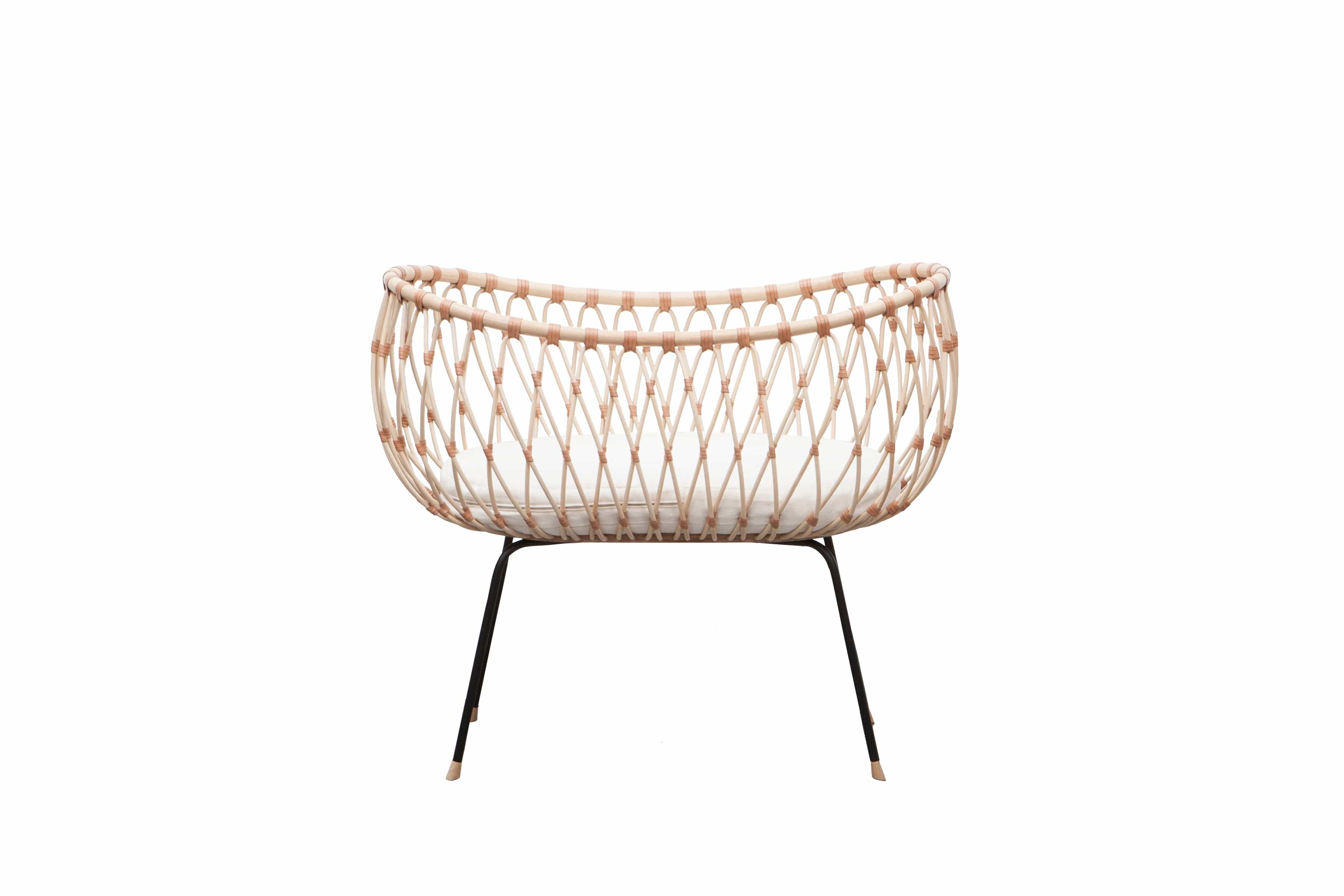 Round crib with outwards curved basket. Made of woven, light beige rattan beams, connected with light brown leather straps and standing on slim black metal legs. 