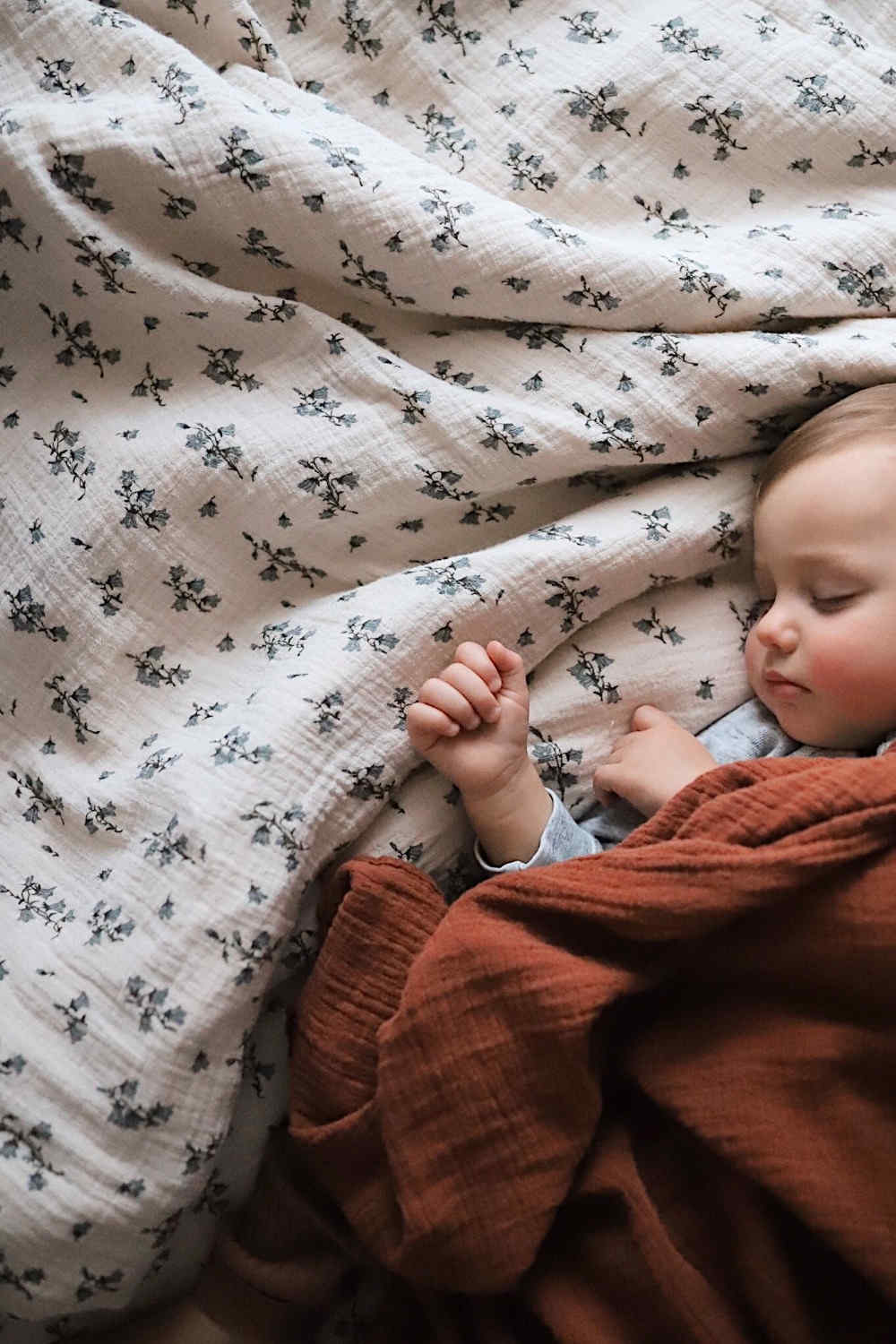 A baby lying on cotton bedding in color rosa with bell flowers print